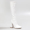 The La Gogo Calf Boot in White Wet Look showcases a chic knee-high silhouette with a chunky block heel. Crafted from vegan patent material, it features a smooth, shiny finish with a rounded toe, exuding minimalist elegance against a light gray background.